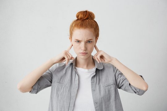 Portrait of angry and annoyed young female frowning and plugging her ears with fingers can't stand loud noise or ignoring stressful unpleasant situation or conflict. negative human emotions