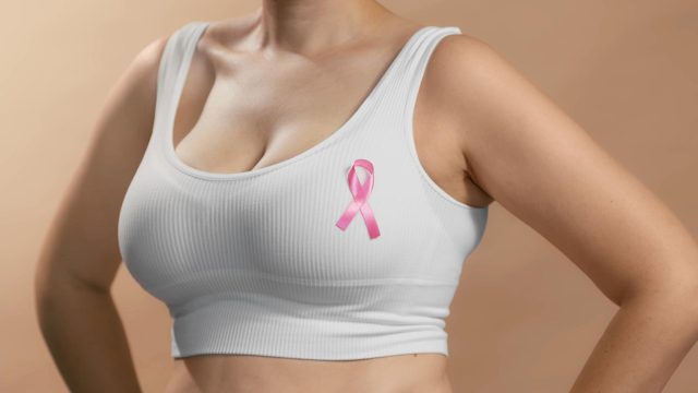 Young lady in a white top with a ribbon sign on her chest to support pink october and females combating breast cancer anonymous studio shot photo on beige background
