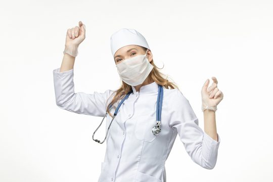 Front view female doctor in medical suit with sterile mask due to coronavirus dancing on the white wall illness pandemic health covid-