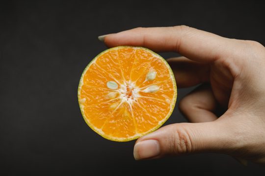 Crop anonymous female demonstrating fresh juicy fruit containing vitamins and macroelement for healthy lifestyle on black background