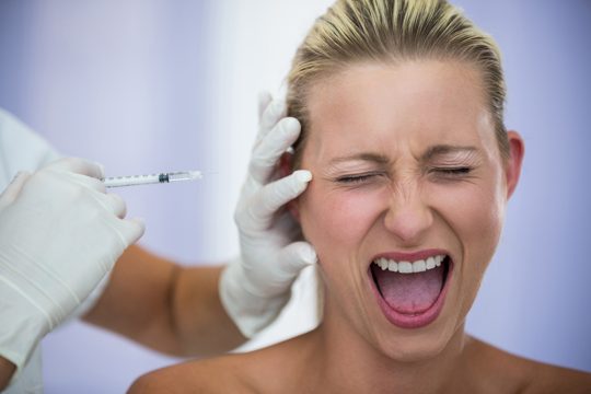 Scared woman shouting while receiving an injection from cosmetic treatment
