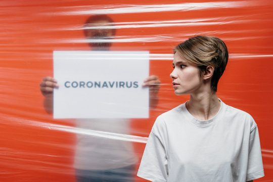 Woman in White Crew Neck T-shirt Standing Beside A Man Holding A Placard Of Coronavirus