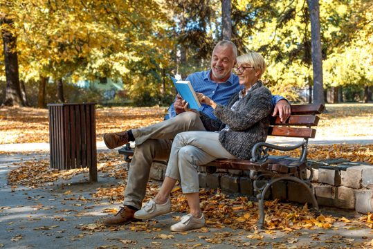 Caucasian elderly couple sitting on a bench and reading a book in the park