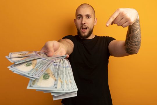 Strict young handsome guy wearing black shirt holding and points at cash