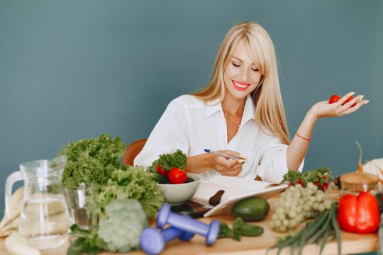 Beautiful girl make a salad. sporty blonde in a kitchen. woman writing recipe in notebook.