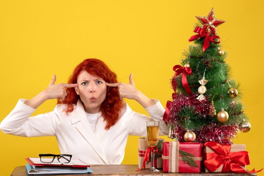 Female worker sitting behind table with christmas presents and tree on yellow