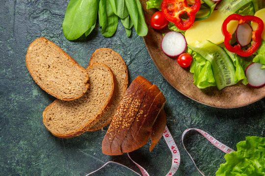 Half shot of black bread slices fresh chopped vegetables on a plate and meters green bundle on dark colors surface