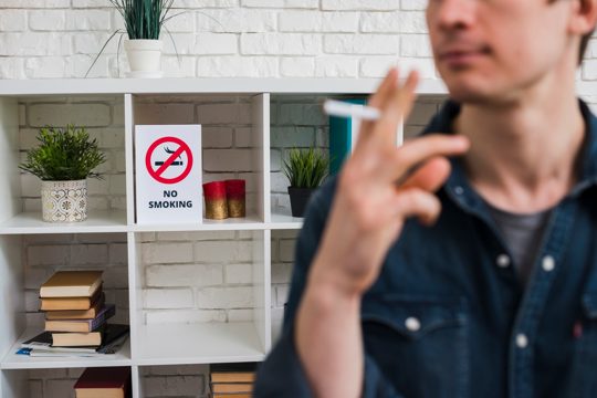 Defocus man with cigarette in front of no smoking poster on shelf