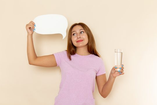 Front view young attractive female in pink t-shirt and blue jeans holding glass of water and white sign