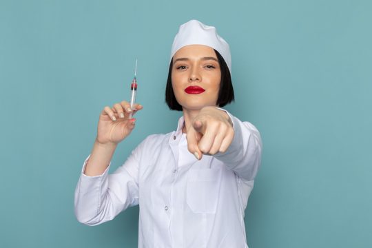 A front view young female nurse in white medical suit holding injection on the blue desk medicine hospital doctor